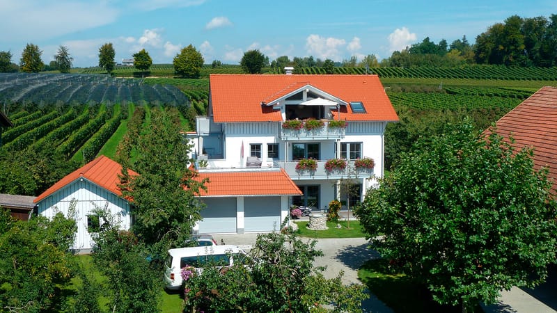 Das Haus am Sonnenbichl mit orangeroten Dächern, dahinter Obstanlagen